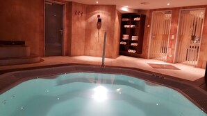 A spa area with a hot tub, tiled walls, and shelves with towels. - Europa Annex (Saas-Fee)