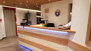 A reception desk with a wooden finish and a textured wall behind it. - Europa Annex (Saas-Fee)