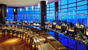 A bar area with seating, a bar counter, and large windows with a city view. - Hilton Baku (Baku)