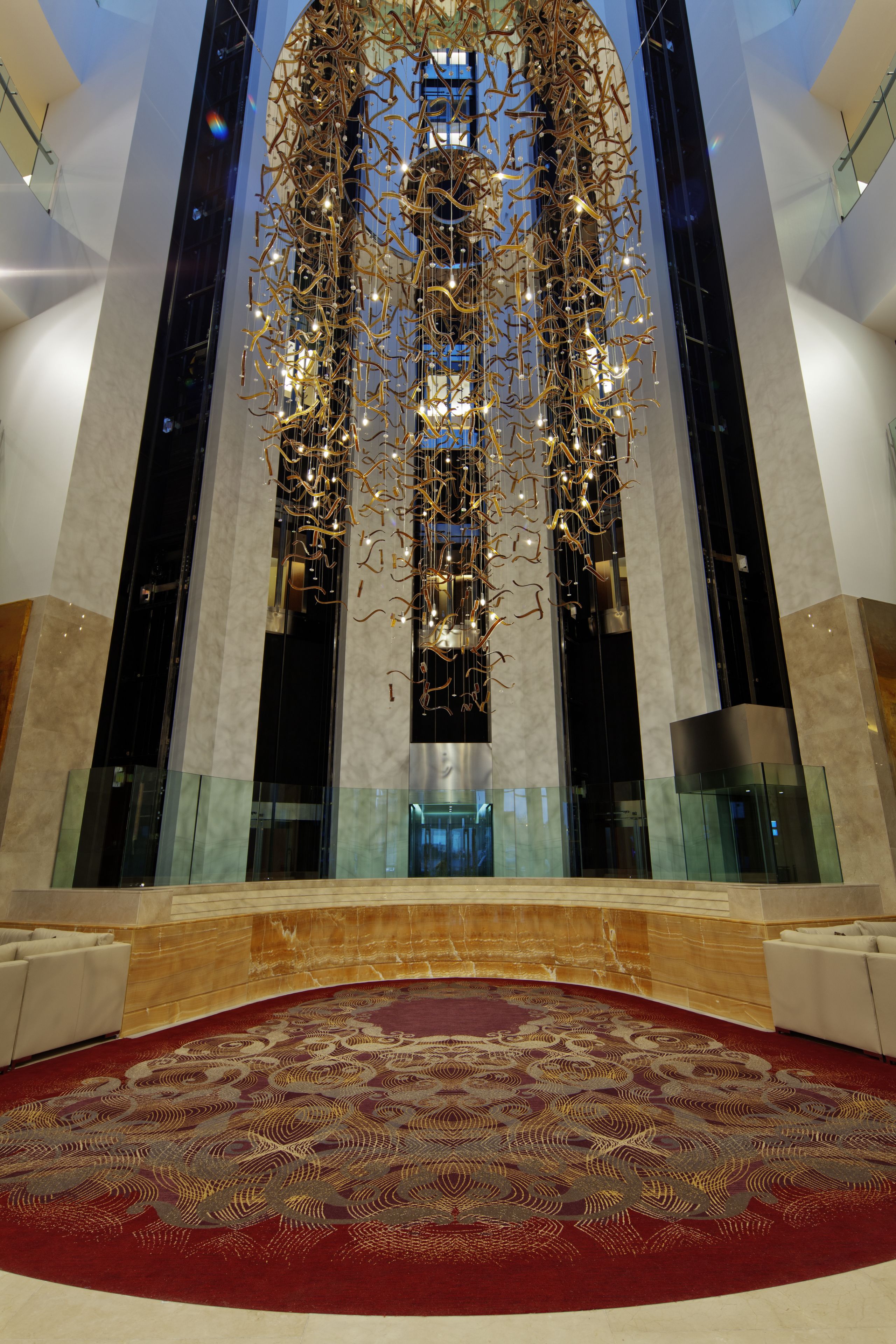 A spacious lobby with a large, ornate chandelier, a patterned carpet, and a high ceiling.