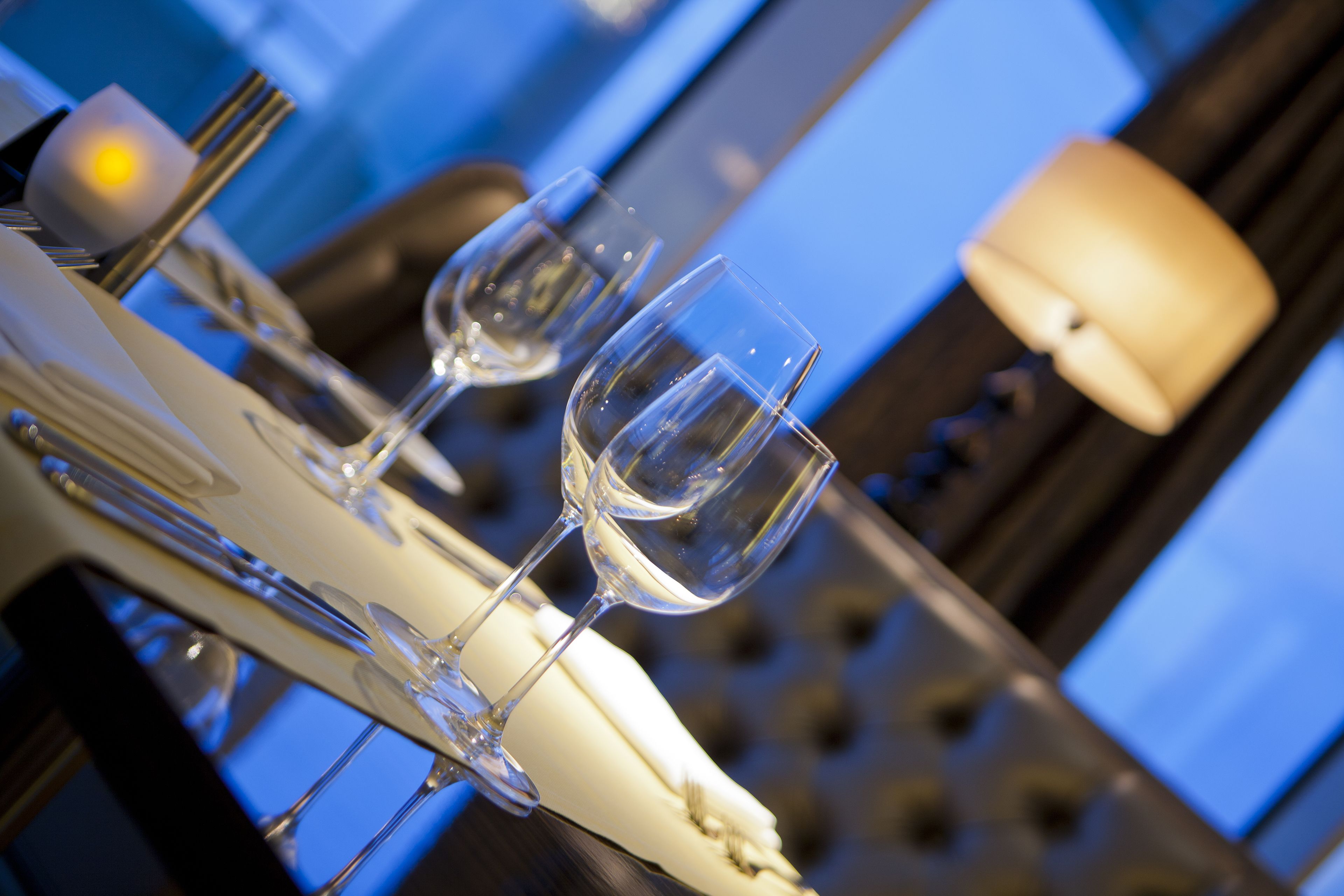 Une table à manger avec des verres à vin et des couverts, placée dans un intérieur moderne sur fond bleu.