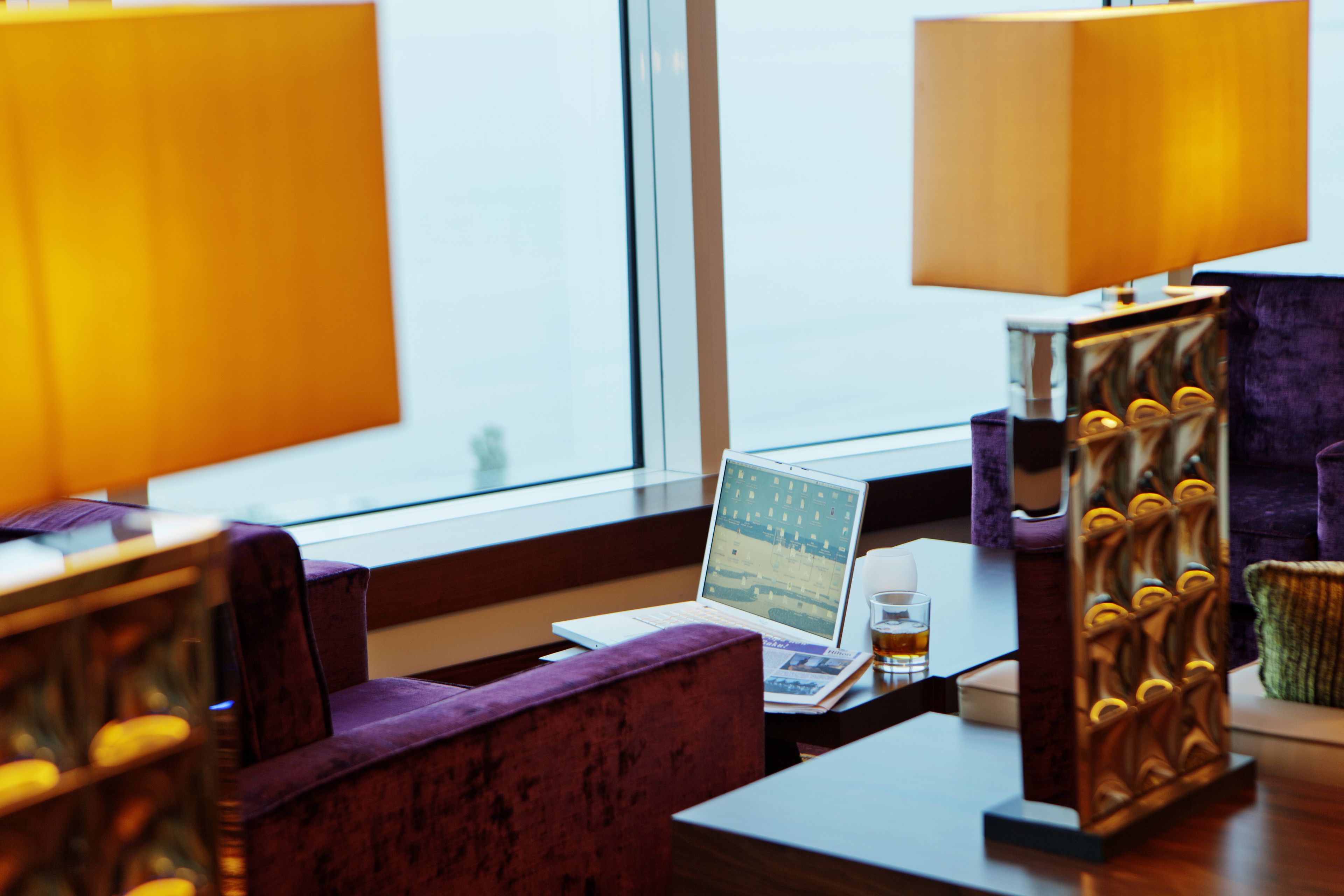 A hotel room with a laptop on a table, a glass of whiskey, and a decorative wooden stand.