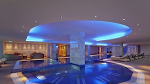 A modern indoor pool area with a central column, lounge chairs, and a seating area with cushions. - Hilton Baku (Baku)