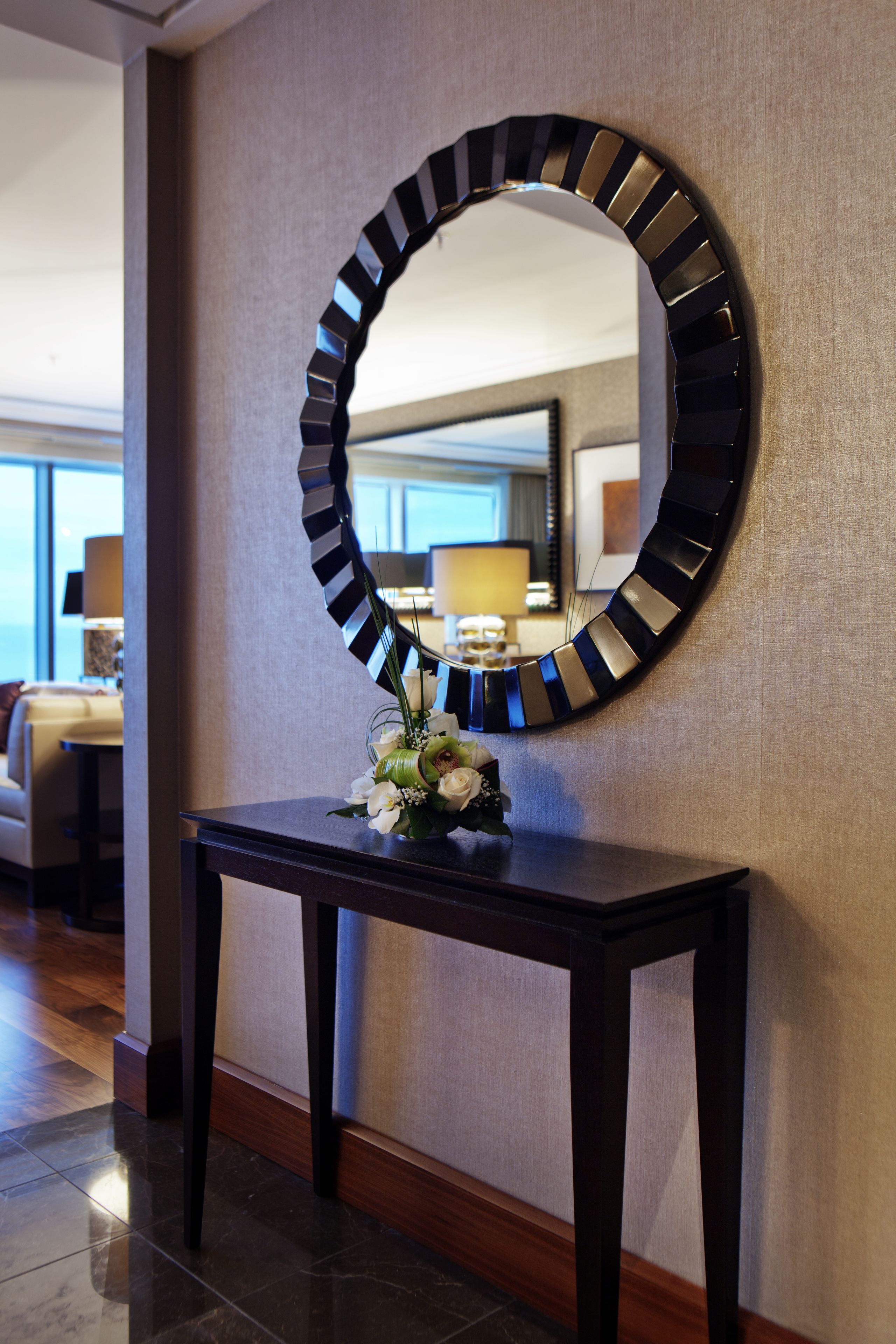 A round mirror with a black and white striped frame on a dark wooden console table.