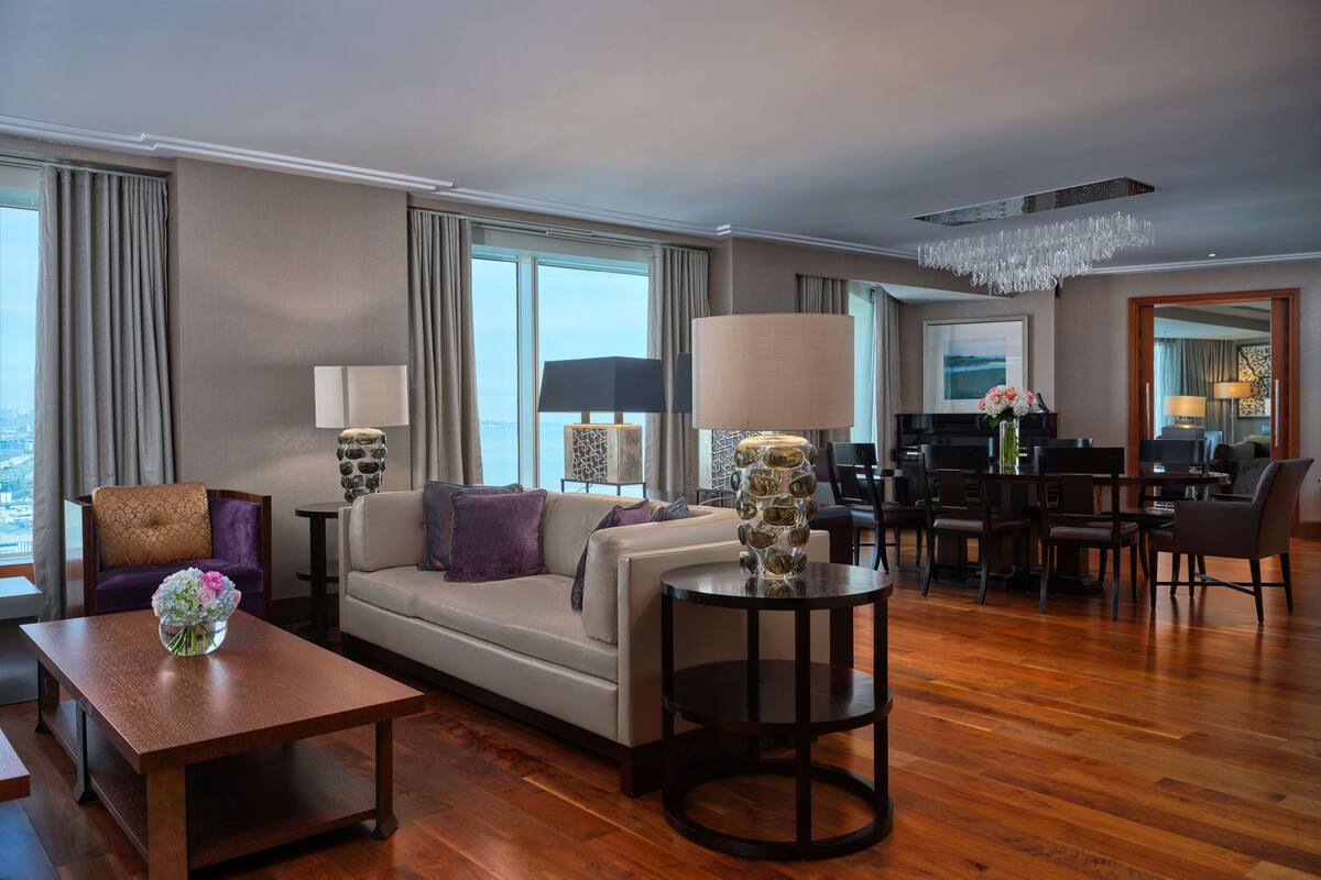 Una habitación de hotel moderna con sofá, sillones, mesa de comedor y una araña.