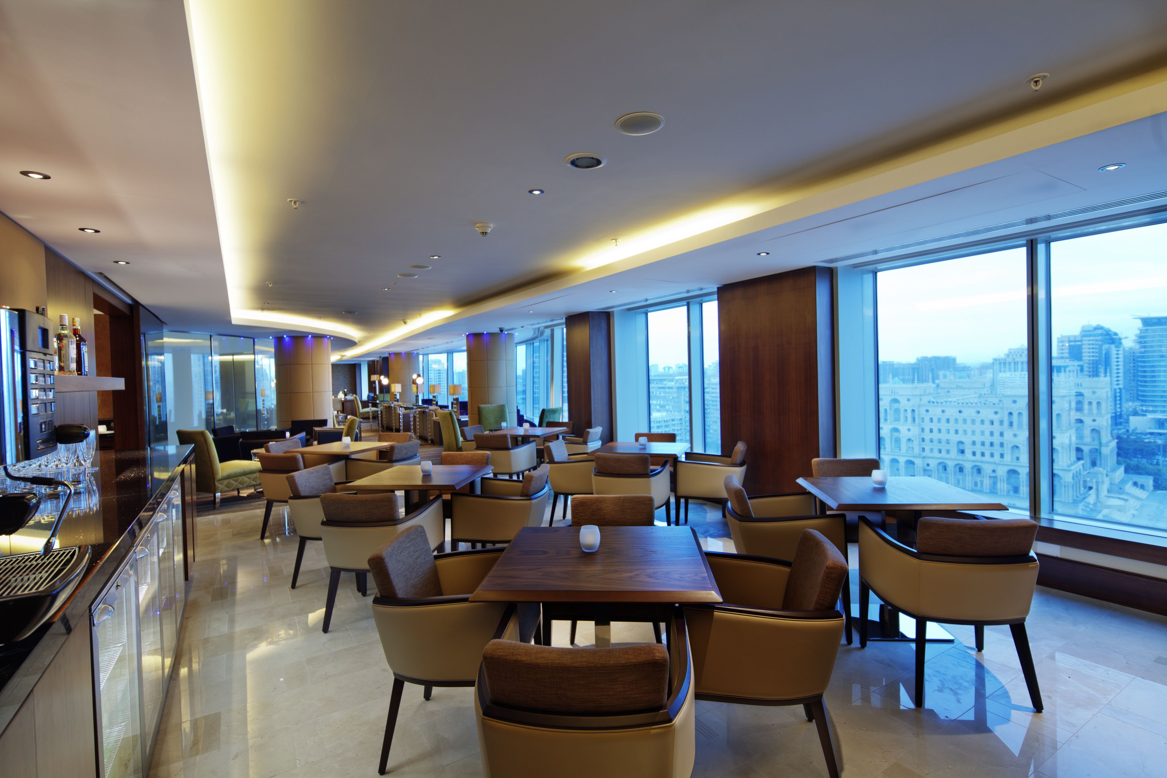 A modern hotel lobby with a bar area, seating arrangements, and large windows offering city views.