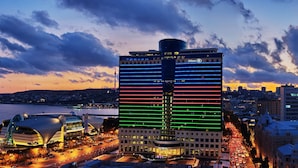A modern hotel with a prominent Hilton sign, surrounded by a waterfront view and a busy street. - Hilton Baku (Baku)