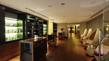 Een moderne hotellobby met houten vloeren, een receptiebalie en een rij rieten stoelen met paarse kussens.