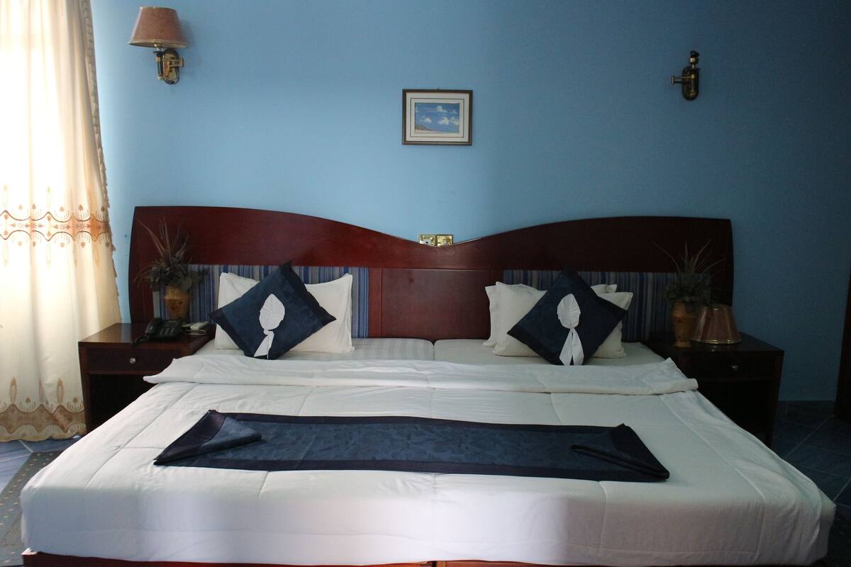 A neatly made bed with a dark throw blanket, a wooden headboard, and two bedside tables with lamps.