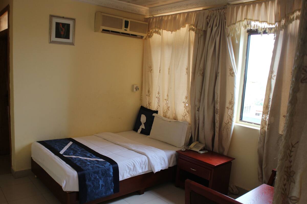 A bedroom with a bed, bedside table, and a window with curtains.