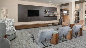 Un salon moderne doté d’un téléviseur à écran plat, de fauteuils recouverts d’un tissu gris, de petites tables d’appoint en bois et d’un tapis à motifs.
