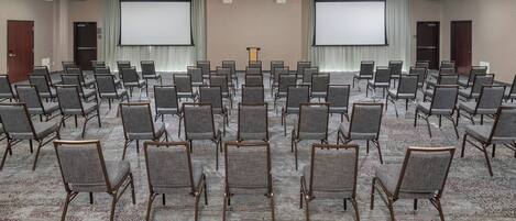 A conference room with rows of chairs, a projector screen, and a podium.