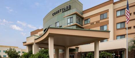 A Courtyard by Marriott hotel with a covered entrance, multiple floors, and an American flag.