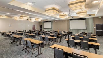 A conference room with multiple tables and chairs, a large screen, and a projector.