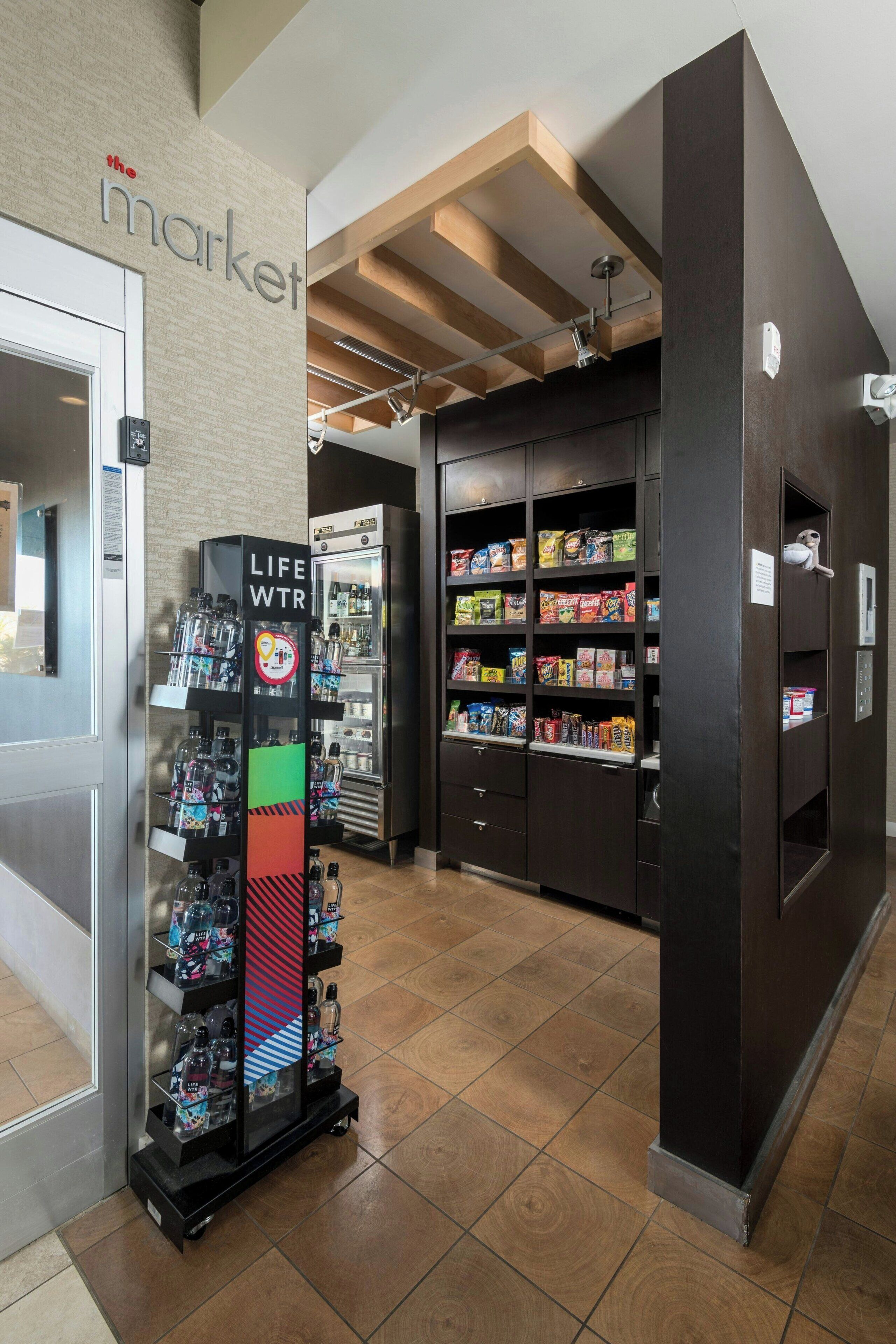 Een winkelinterieur met schappen vol snacks en dranken, een koeltoog en een automaat.