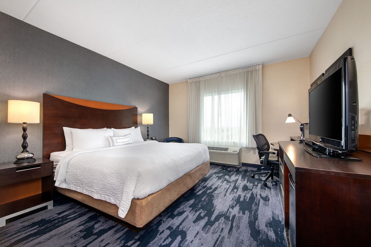 A hotel room with a large bed, a desk with a television, and a chair.