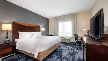 Quarto de hotel com uma cama grande, uma escrivaninha com televisão e uma cadeira.