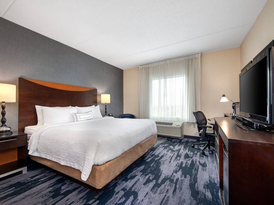Quarto de hotel com uma cama grande, uma escrivaninha com televisão e uma cadeira.