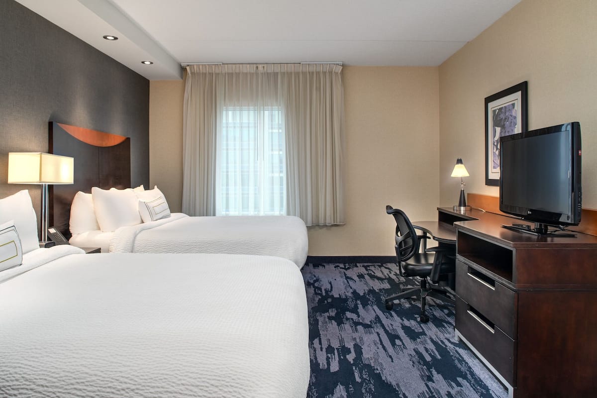 A hotel room with two beds, a desk, a television, and a window with curtains.