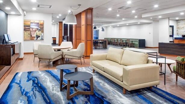 A modern hotel lobby with a seating area, a reception desk, and a dining area. - Fairfield Inn & Suites by Marriott Toronto Mississauga (Mississauga)