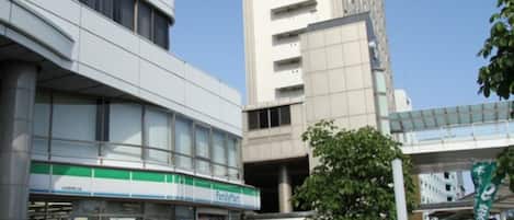 A FamilyMart convenience store with a modern building facade, a parking area with bicycles, and a pedestrian walkway.
