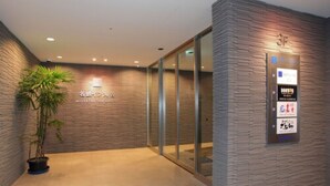 A reception area with a modern design, featuring a reception desk, a potted plant, and a wall-mounted information board. - Meitetsu Inn Kariya (Kariya)
