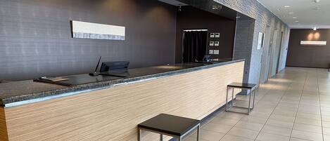 A modern reception desk with a wooden finish and a glass top, accompanied by a small stool.