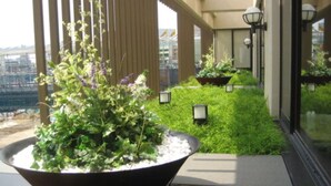 A balcony with a large planter, green plants, and a view of a bridge. - Meitetsu Inn Kariya (Kariya)