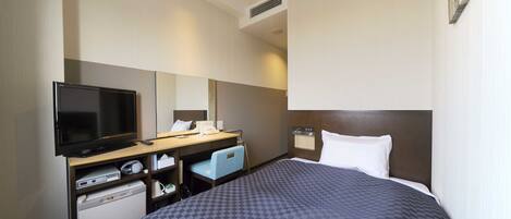 A hotel room with a bed, a desk with a television, a mirror, a small kitchenette, and a window.