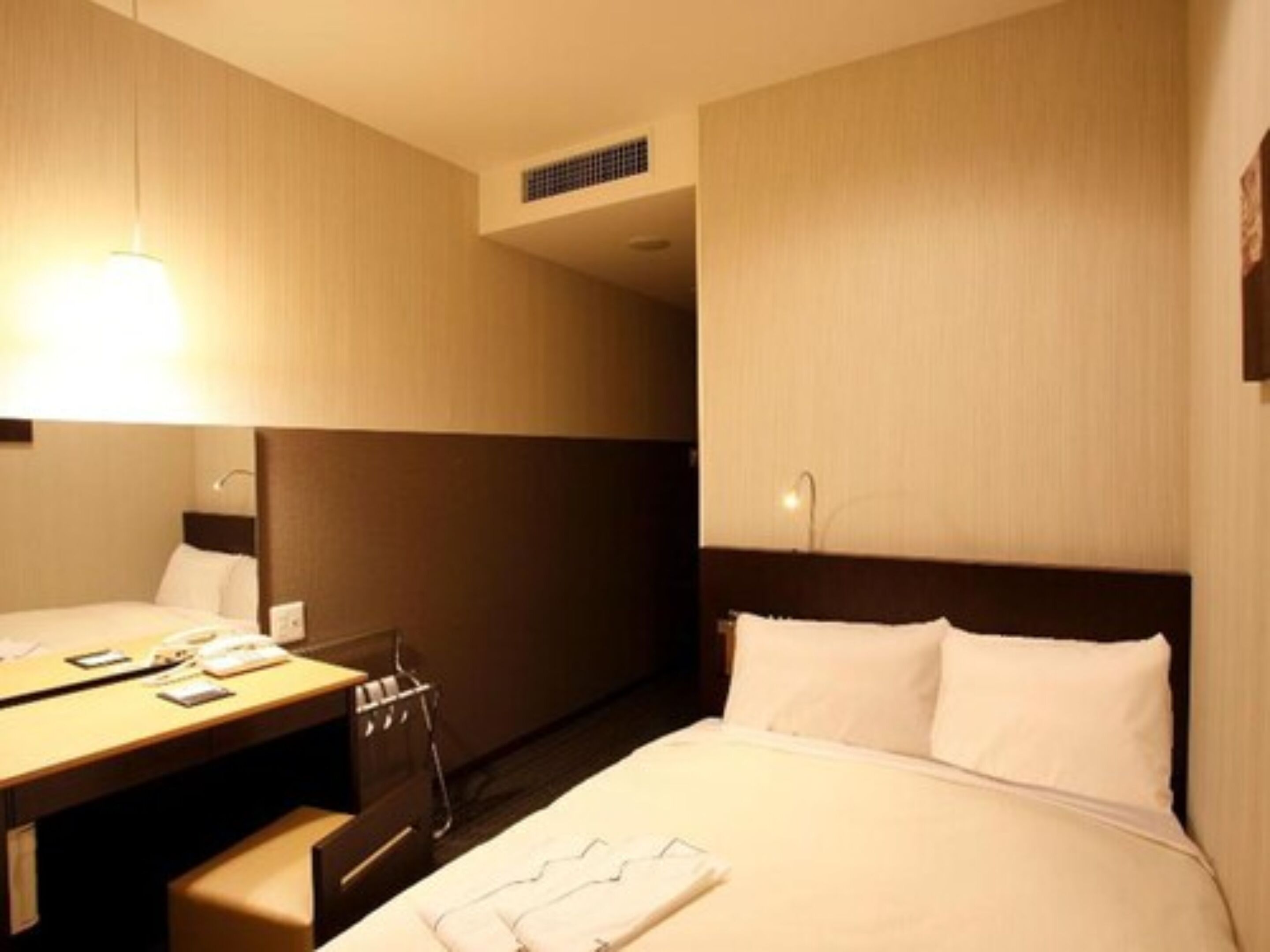 Habitación de hotel con cama, escritorio y silla. Hay un espejo en la pared y una ventana.