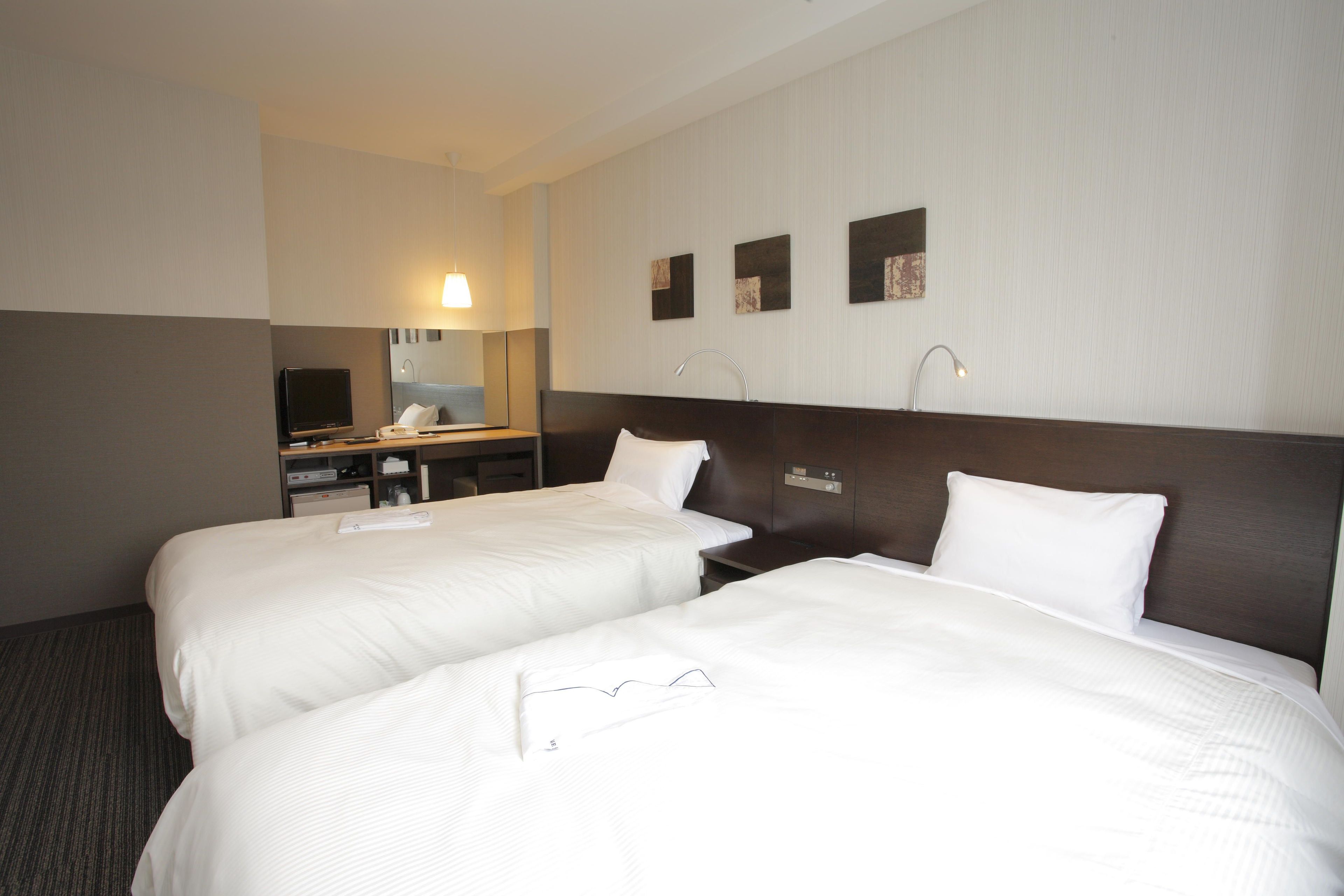 A hotel room with two beds, a desk, a television, and a mirror.