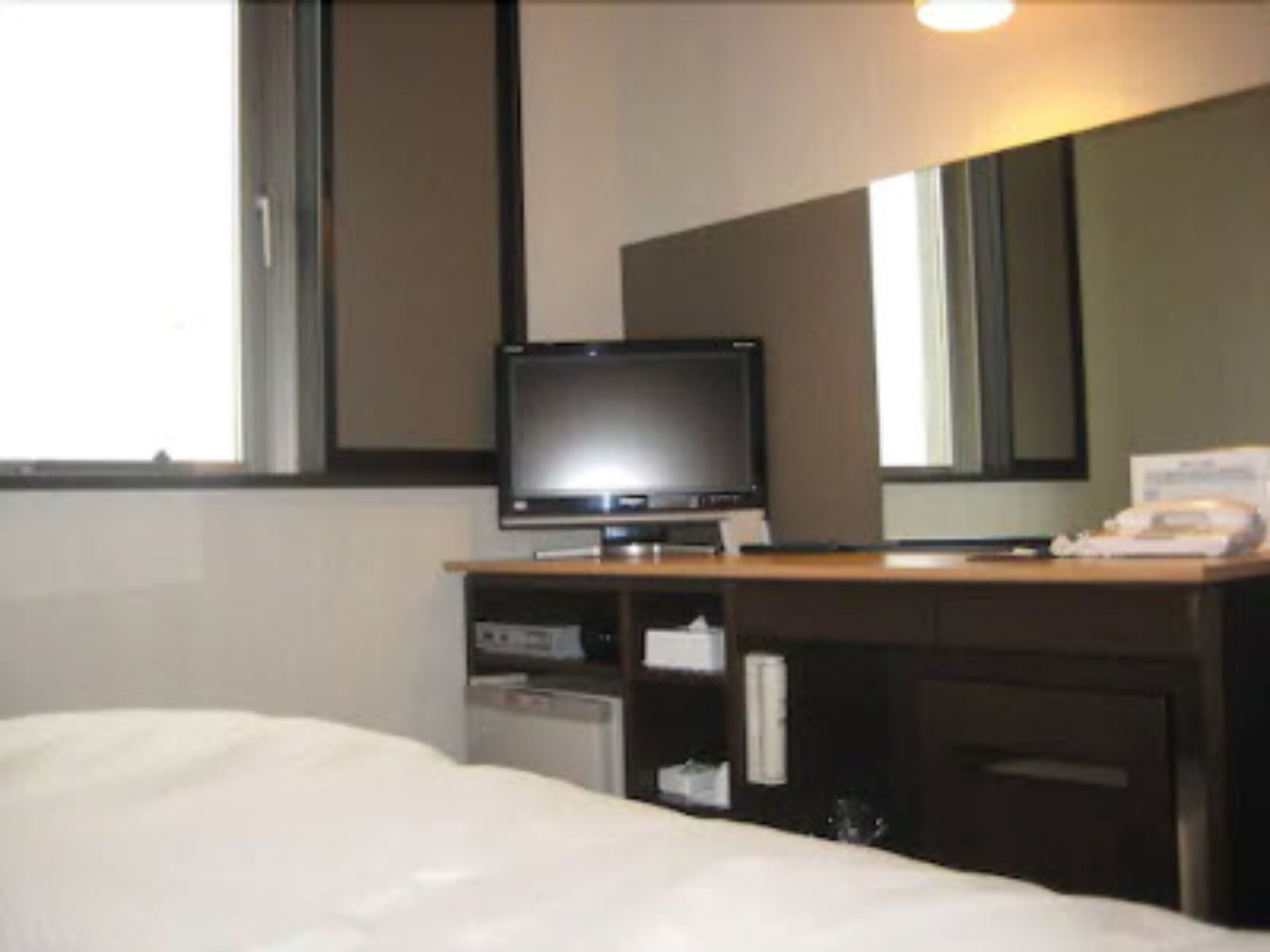 A hotel room with a bed, a television on a wooden stand, a desk with a telephone, and a mirror on the wall.