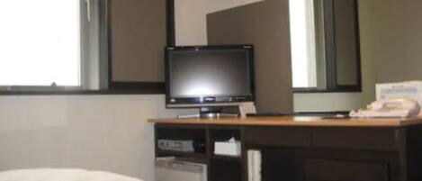 A hotel room with a bed, a television on a wooden stand, a desk with a telephone, and a mirror on the wall.