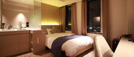 Ein Hotelzimmer mit einem großen Bett, einem Schreibtisch, einem Spiegel und Blick auf die nächtliche Stadt.