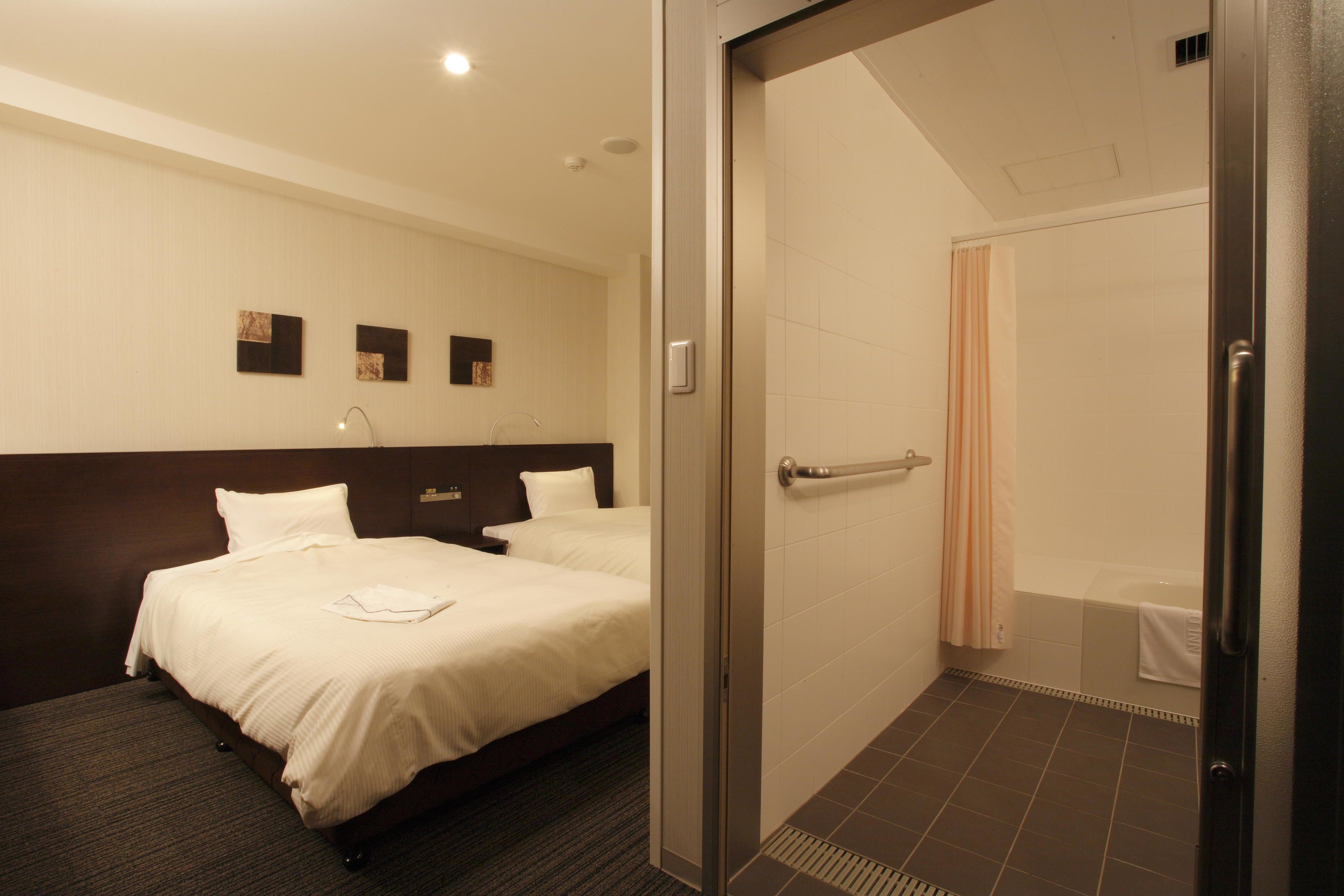 A hotel room with a bed, a shower, and a door leading to the bathroom.