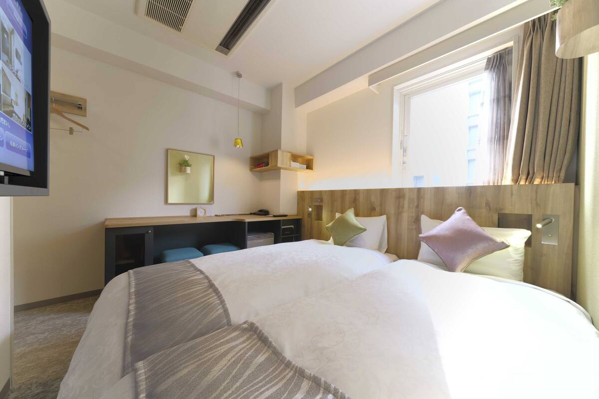 A hotel room with a large bed, a desk, a chair, a TV, and a window with curtains.