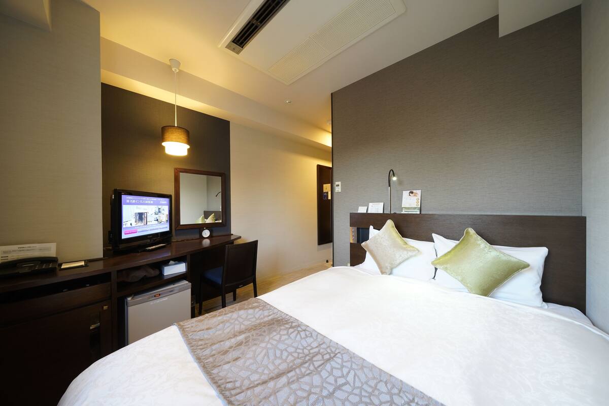 A hotel room with a bed, a desk with a computer, a chair, and a small refrigerator.