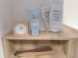 A wooden shelf with a clock, a spray bottle, and a pair of slippers.