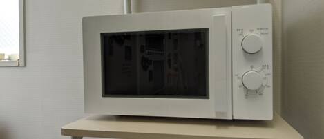 A white microwave on a white stand in a room with plain walls and a window.