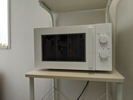 A white microwave on a white stand in a room with plain walls and a window.