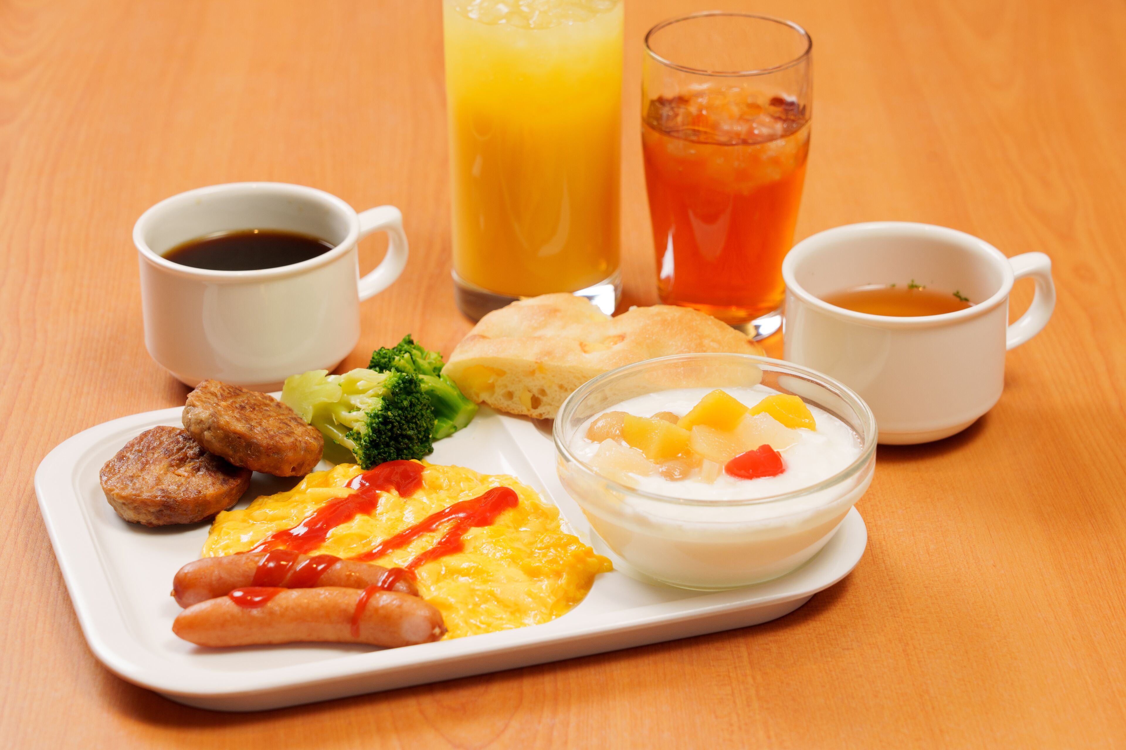 A breakfast tray with eggs, sausage, toast, and a glass of orange juice.