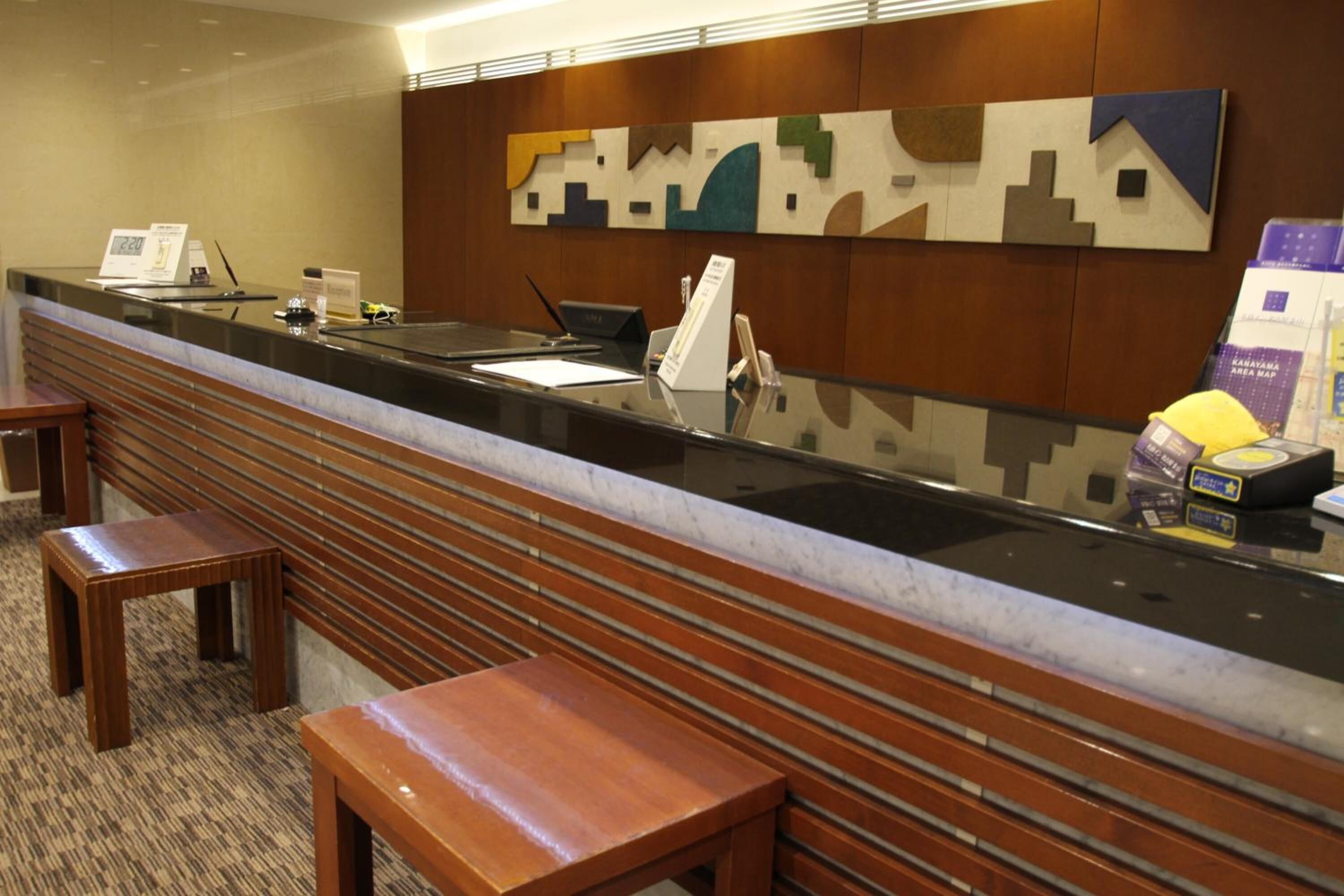A hotel reception area with a marble counter, wooden benches, and a wall-mounted abstract art piece.