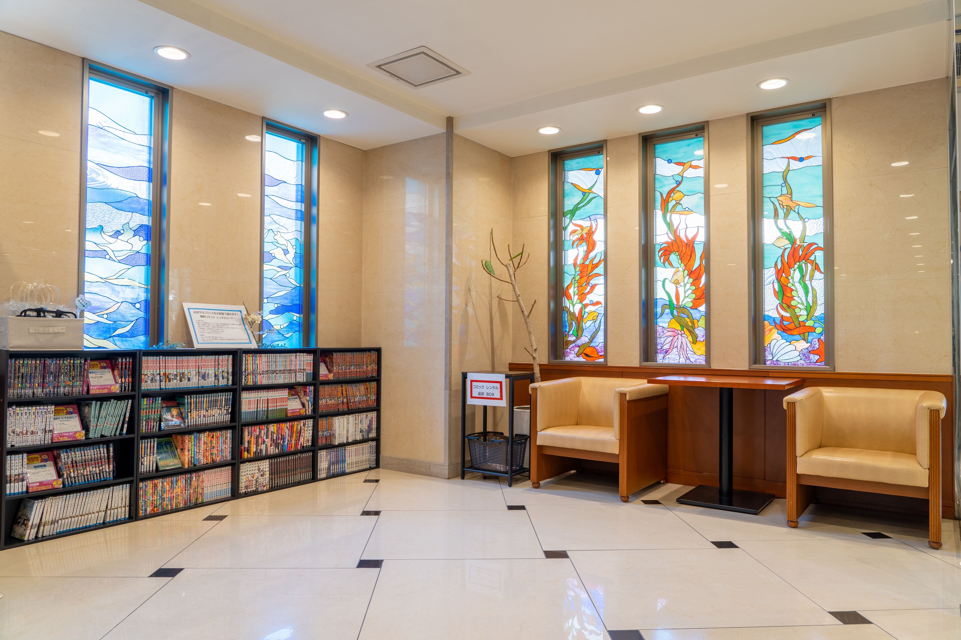 A reception area with a bookcase, two chairs, and stained glass windows.