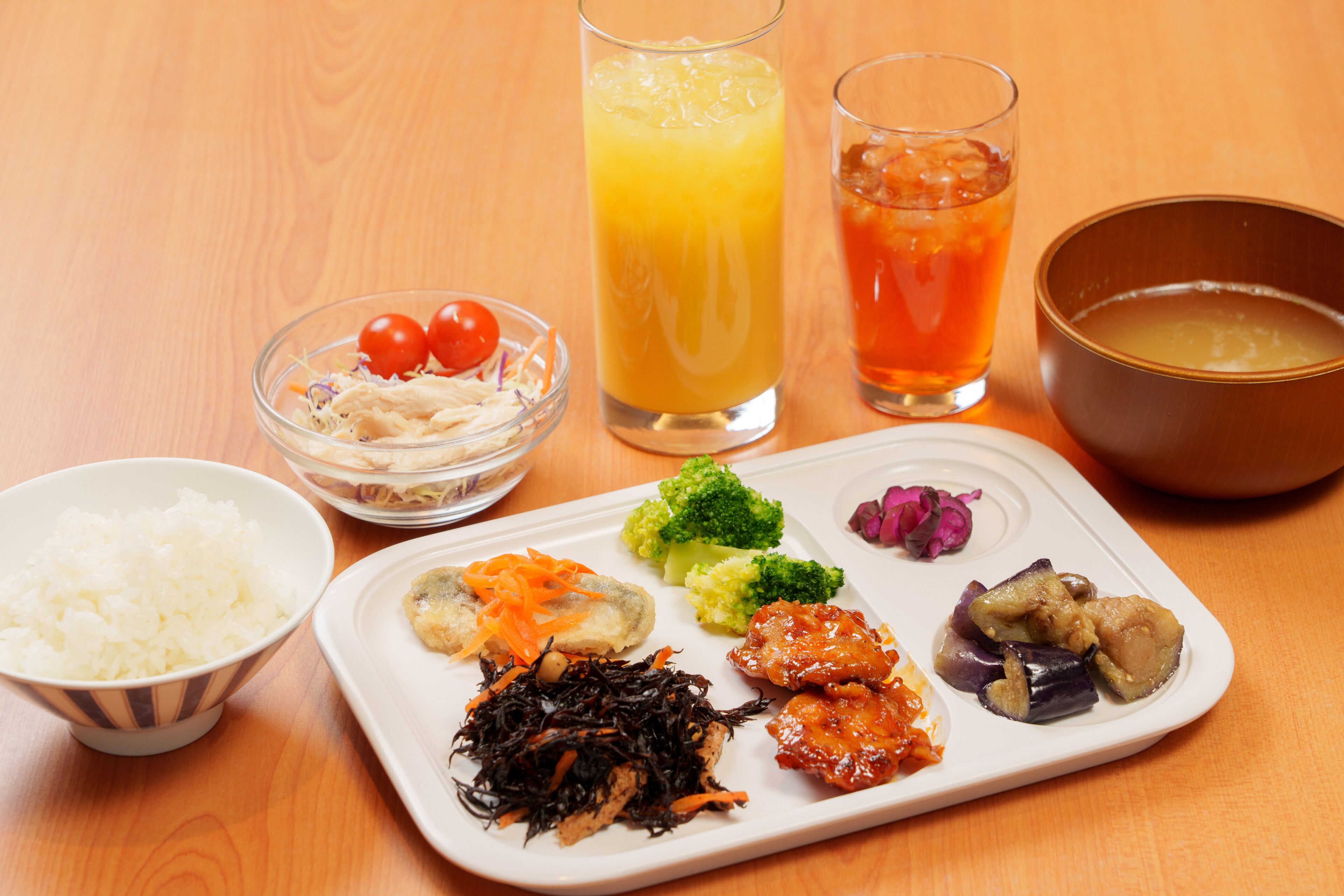 A meal with rice, vegetables, and a soup bowl on a wooden table.