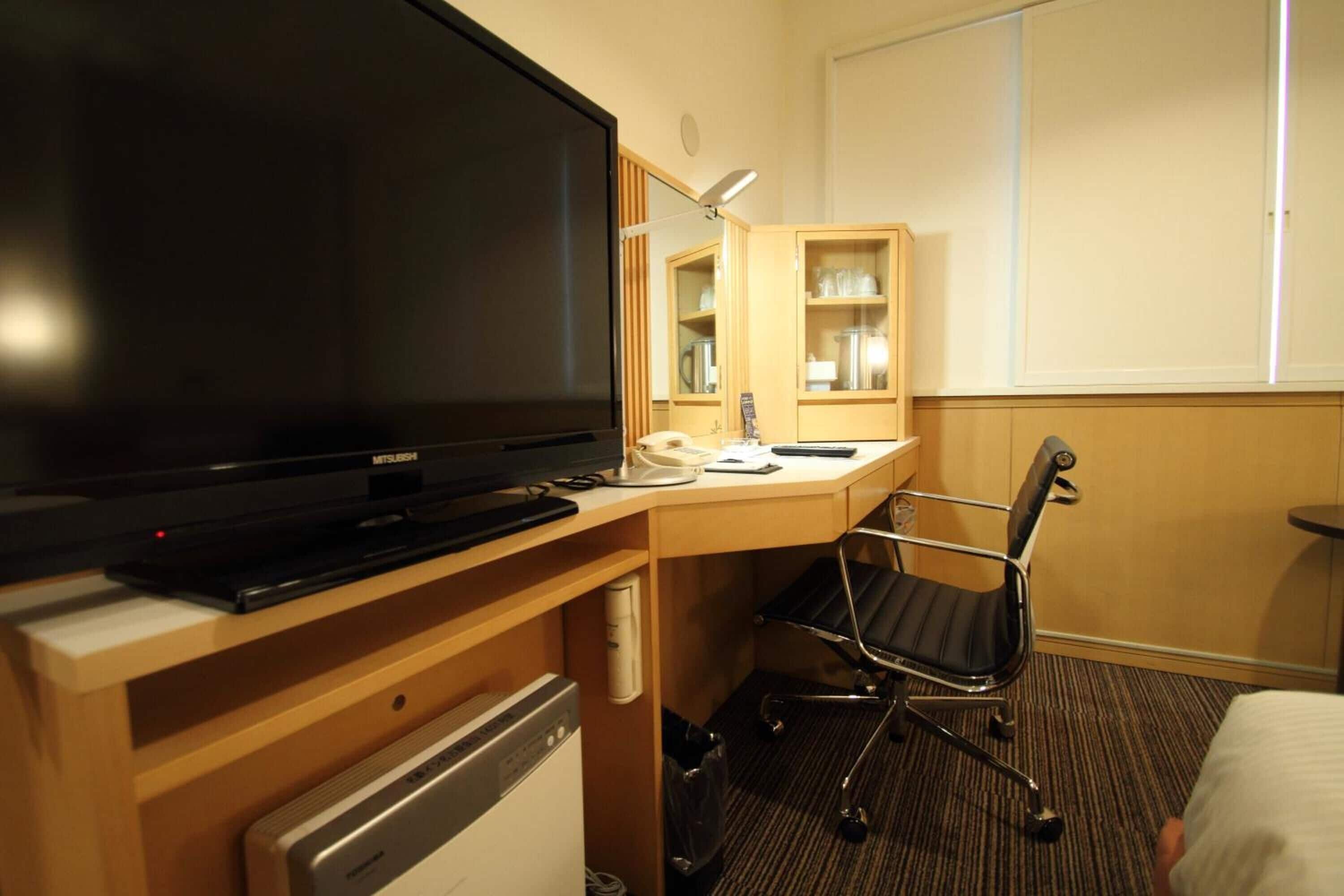 Habitación de hotel con una televisión de pantalla plana grande, un escritorio con una silla, un espejo y una cama.