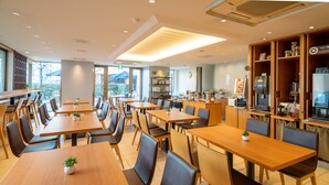 A modern restaurant interior with multiple wooden tables and chairs, a kitchen area with appliances, and a view of the outdoors. - Meitetsu Inn Nagoya Kanayama (Nagoya)