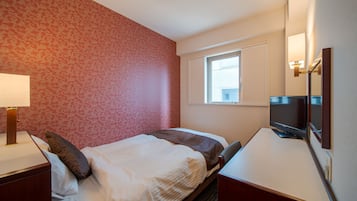 Una habitación de hotel con una cama, un escritorio con televisor, una ventana y una lámpara.