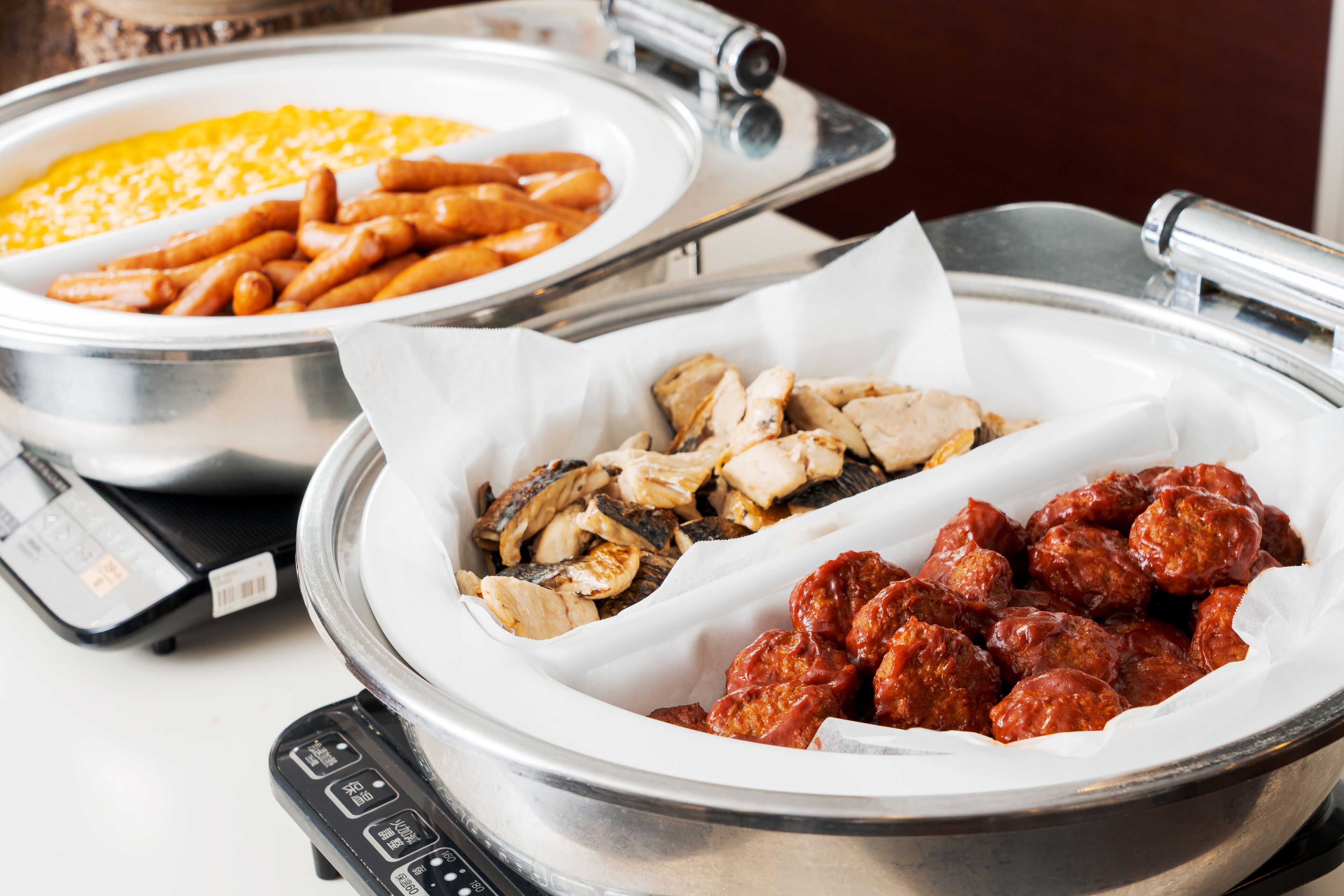 A buffet with various food items including sausages, chicken, and meatballs.