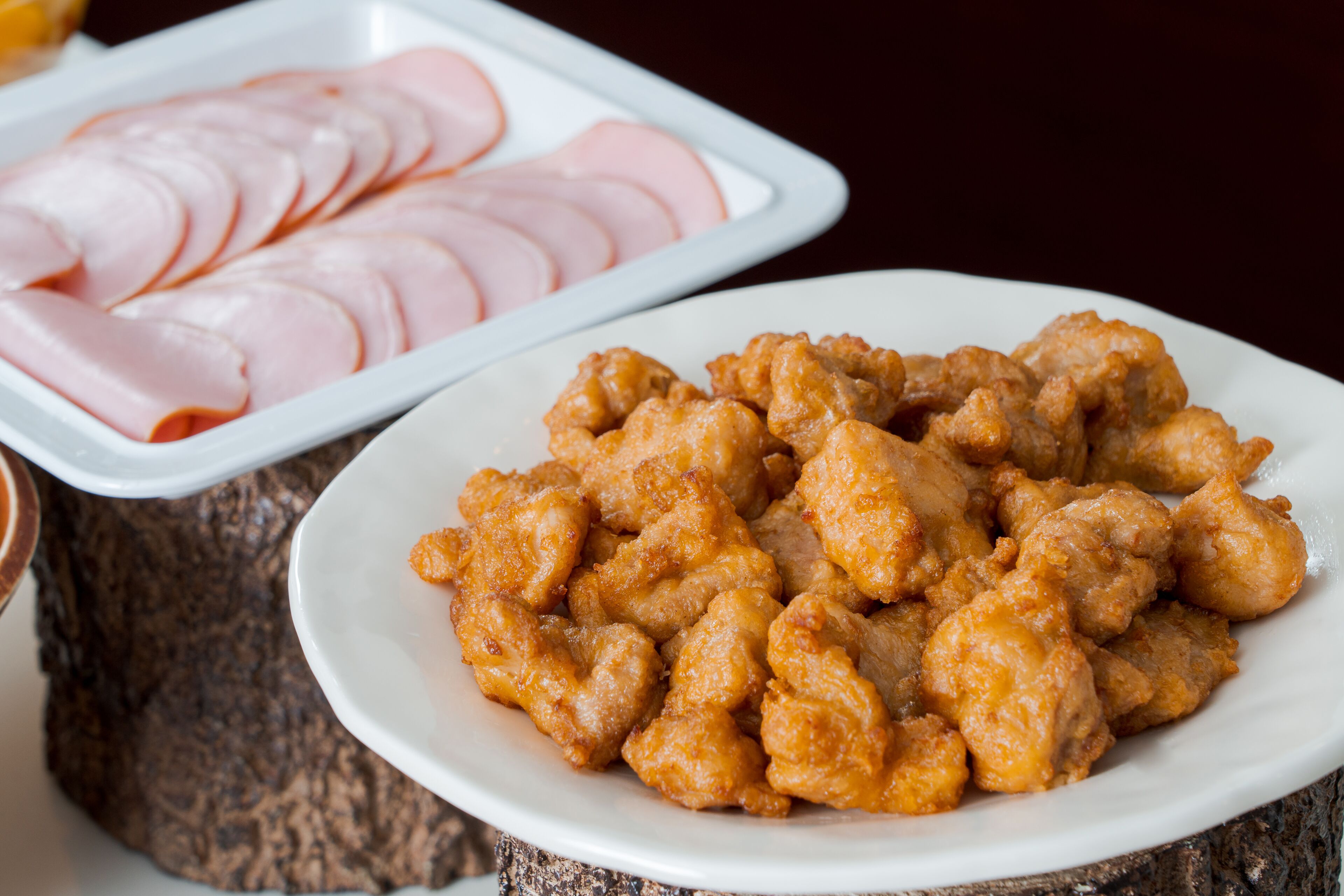 A plate of fried chicken and sliced ham on a wooden table.