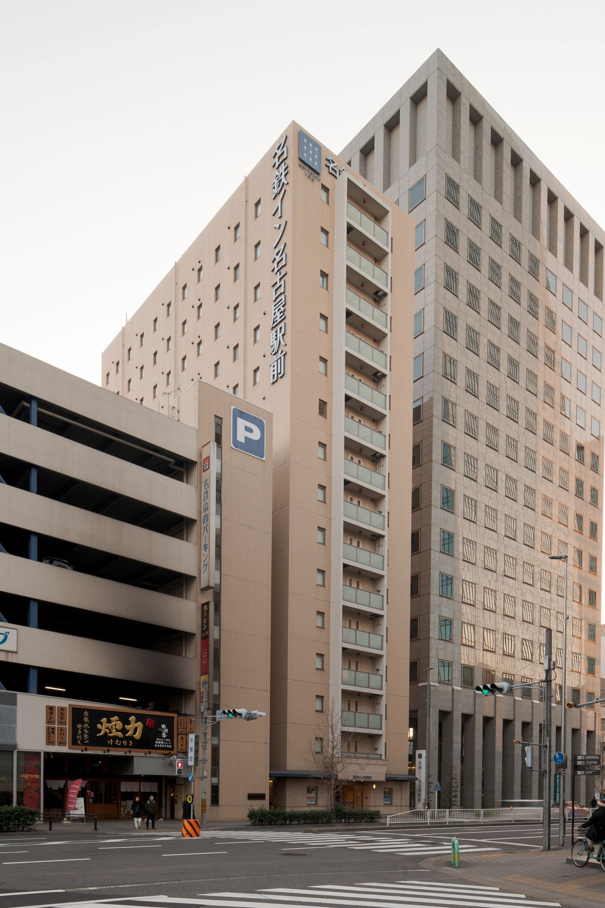 Un edificio de varios pisos con un estacionamiento en la planta baja, un letrero con caracteres japoneses y un paso de peatones.